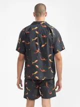 Camisa de manga corta con cuello estilo camper y estampado de sirenas en tonos naranja y amarillo. Tiene botones de madera y parche con logo. Corte boxy.