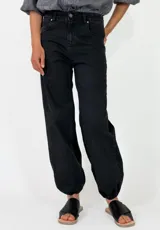 Pantalon de denim azul oscuro con diseño abombado y puños fruncidos con elástico en los tobillos. Cuenta con bolsillos laterales y cierre frontal con botón y cremallera.
