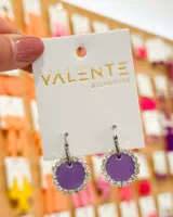 Aros colgantes con aro de acero plateado y dije circular color lila con borde de strass plateado.