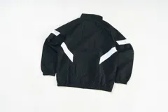 Campera deportiva unisex confeccionada en nylon liviano color negro con paneles diagonales blancos en las mangas y micrográficos Kaboa aplicados al frente. Tiene calce relajado y estructura clásica.