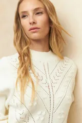 Polera blanca de punto con cuello alto, manga larga y calados decorativos.