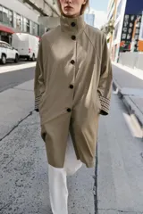 Trench de corte oversize color beige, con cuello alto, cierre frontal de botones y mangas largas con puños vueltos estampados a cuadros. Cuenta con bolsillos delanteros de vivo.