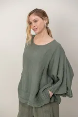 Blusa de lino color verde militar, holgada, de manga 3/4 con volados en los puños, cuello redondo y detalle de alforzas horizontales en el dobladillo.