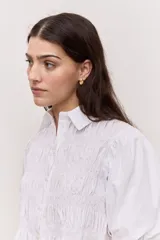 Camisa azul marino de cuello clásico, mangas abullonadas a tres cuartos y detalle fruncido en el frente. Presenta una silueta amplia y diseño corto con vuelo en el ruedo.