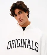 Buzo boxy de algodón y poliéster en color blanco, con cuello alto y medio cierre frontal. Presenta un diseño amplio con mangas largas, puños y ruedo en rib, y un bordado frontal con el texto "ORIGINALS" en color negro.