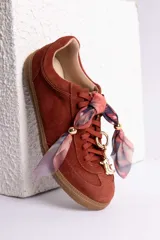 Zapatillas de gamuza color marrón con suela de goma color caramelo. Presentan cordones al tono y un detalle decorativo de pañuelo estampado atado en los laterales con esferas metálicas doradas.