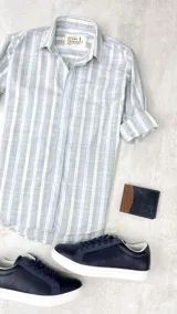 Camisa de manga larga con cuello clásico y cierre con botones. Diseño a rayas verticales en gris, celeste y blanco.