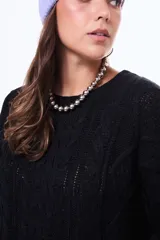 Buzo tejido de punto con diseño de trenzas, color negro, de corte holgado, cuello redondo y mangas largas.