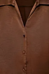 Camisa corta de tejido satinado color marrón, con cuello solapa, escote en pico y manga larga. Presenta cierre frontal con botones forrados a tono.