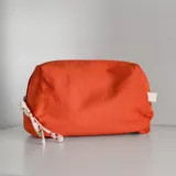 Neceser de tela color coral con cierre superior y detalle de etiqueta de cuero con logo de la marca.