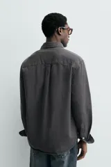 Camisa de corte relajado confeccionada en una mezcla de lyocell y algodón con efecto lavado. Presenta cuello solapa, manga larga con puños abotonados, bolsillo de plastrón en el pecho y cierre frontal con botones.