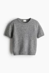 Buzo de punto fino color gris jaspeado, con cuello redondo y mangas cortas. Presenta remates acanalados en el cuello, puños y bajo.