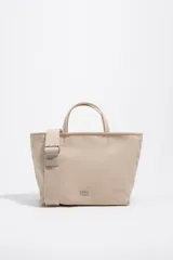 Bolso shopper mediano de mano Bimba y Lola color marrón, confeccionado en poliamida con detalles en cuero y herrajes metálicos dorados. Cuenta con doble asa de mano, correa de hombro ajustable de lona beige, cierre superior con cremallera y logo impreso en dorado al frente.