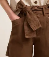 Short corto de sarga en color beige, con tiro medio, bolsillos laterales y cinturón incorporado del mismo tejido para atar en la cintura.