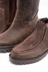 Bota corta de cuero vacuno en tono marrón oscuro, con diseño de costuras visibles en el empeine y suela de goma dentada tipo track.