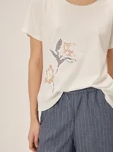 Remera negra de manga corta con cuello redondo y detalle de bordado floral en tono tostado en la parte inferior derecha.