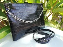 Sobre plateado de cuero con textura, cierre superior y cadena metálica decorativa. Incluye correa de cuero desmontable y regulable.