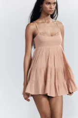 Vestido corto negro de gasa con escote recto y tirantes finos ajustables. El corpiño tiene fruncido elástico y el ruedo es escalonado con volados. Presenta un detalle de encaje a tono en el borde del escote.