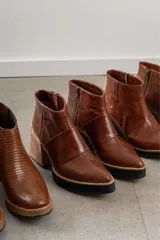 Botineta de cuero negro con diseño combinado en cuero charolado, plataforma y taco cuadrado de madera clara. Presenta cierre lateral y puntera redondeada.