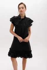 Vestido corto de lino color negro, con silueta recta y largo por encima de la rodilla. Incluye un cuello removible con volados y lazo, y detalles de volados en las sisas y el ruedo.