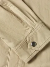 Campera tipo Harrington de algodón color beige claro, con cuello camisero y cierre frontal de cremallera. Presenta bolsillos laterales ribeteados y el logo de Tommy Hilfiger bordado en el pecho.