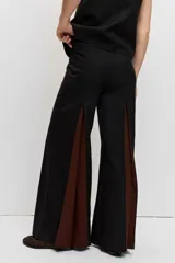 Pantalón sastrero de corte ancho y tiro alto, color negro con inserciones laterales en tono marrón que forman godets.