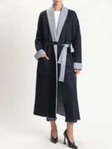 Saco largo de tejido de punto color negro con micro lentejuelas plateadas. Presenta cuello y solapas en contraste de color gris jaspeado, puños doblados en gris y un lazo para ajustar a la cintura.