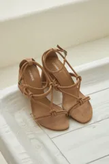 Sandalias color nude confeccionadas en cuero nobuk, con taco cuadrado y tiras finas con nudos en el empeine y ajuste de pulsera en el tobillo.