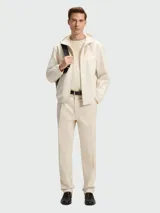 Chaqueta ligera con capucha, cierre frontal y puños elásticos, color beige claro. Presenta un diseño con costuras en forma de chevron en el pecho.