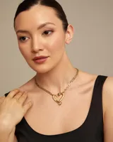 Collar dorado con cadena de eslabones alargados y dije central con forma de corazón estilizado, con la inscripción "UND & 50" en la parte inferior.