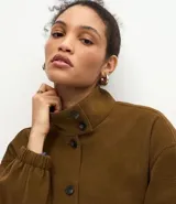 Campera de poliuretano texturizado color marrón, con cuello alto, cierre frontal con botones, mangas largas con puños elásticos y ruedo con elástico.