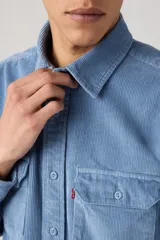 Camisa de pana color azul claro, con cuello clásico, cierre frontal de botones y dos bolsillos con solapa en el pecho.