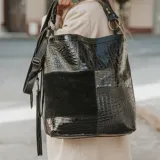 Bolso tipo tote negro con paneles de cuero texturizado y gamuza. Tiene doble asa corta y correa larga ajustable. Cuenta con bolsillos verticales con cierre en ambos lados, bolsillo trasero con cierre y forro interior con bolsillo con cierre y bolsillo para celular.