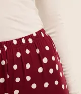 Conjunto de pijama largo de dos piezas: blusa lisa de canalé color blanco con mangas largas y botones en el puño; y pantalón de lunares color borgoña con cintura elástica y puños ajustados.