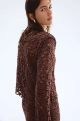 Blusa de manga larga en encaje marrón oscuro con patrón floral. Presenta escote redondo y un borde festoneado en el bajo.