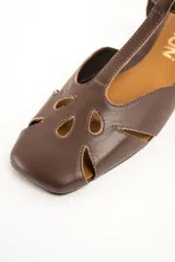 Sandalias planas de cuero marrón, con diseño calado en la puntera, tira en T y tira ajustable al tobillo con hebilla metálica dorada.
