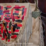 Cartera bandolera de cuero tostado, de formas redondeadas, decorada con flecos y arte pintado a mano en tonos rojos, negros y dorados. Cuenta con correa ajustable para usar al hombro o como bandolera y herrajes en terminación oro viejo.