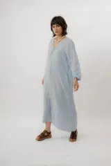 Vestido largo de lino color tostado, de manga larga, con escote redondo y diseño amplio y fresco. Cuenta con un delicado bordado en la espalda con motivos marinos y la frase "no se lo digas".
