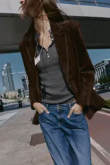 Blazer de piel 100% color marrón oscuro, con cuello solapa, manga larga con hombreras y bolsillos delanteros con solapa. Presenta pespuntes decorativos en contraste y cierre frontal con un botón.