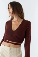 Top tejido de punto con diseño cruzado, escote en V y mangas largas. Cuenta con tiras para anudar en la cintura y detalle de grifa de cuero.