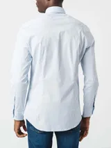 Camisa Tommy Hilfiger de algodón Oxford celeste con microestampado. Tiene corte regular, cuello abotonado, mangas largas con puños abotonados y logo bordado en el pecho.