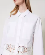 Camisa blanca de popelina de algodón con corte boxy y encaje macramé en el bajo. Presenta cuello clásico, manga larga con sisa caída, puños con abertura y botones, cierre con botones, bolsillos aplicados en la parte delantera y placa con logotipo Oval T en la parte trasera.