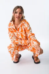 Camisa naranja con estampado floral blanco, de corte holgado, manga larga y cuello camisero.