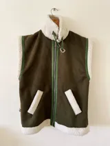 Chaleco negro de cuerina con interior de corderito sintético, bolsillos frontales y hebillas decorativas.