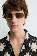 Camisa de manga corta con cuello solapa y cierre frontal de botones, confeccionada en tejido de crochet con patrón de flores en negro y beige.