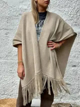 Ruana abierta de lana merino en color beige, con diseño de corte amplio y terminaciones con flecos en el ruedo.