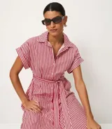 Vestido largo estilo chemise con estampado de rayas rojas y blancas, cuello clásico, cierre frontal con botones y mangas cortas amplias. Incluye un cinto desmontable para ajustar en la cintura.