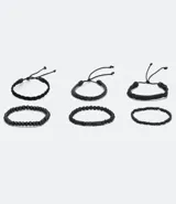 Set de seis pulseras de estilo casual, todas en color negro. Incluye tres pulseras trenzadas ajustables con cordón y tres pulseras con cuentas elásticas (algunas de cuentas lisas y otras de cuentas texturizadas).