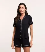 Conjunto de pijama corto negro con ribetes blancos, compuesto por una camisa de manga corta con cuello, bolsillo en el pecho y cierre abotonado, y un short con cintura elástica.