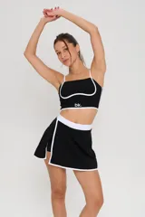 Conjunto deportivo de dos piezas compuesto por un top de tirantes finos con detalle de ribete blanco y logo estampado, y una pollera short con cintura elástica blanca y tajo lateral con ribete blanco.